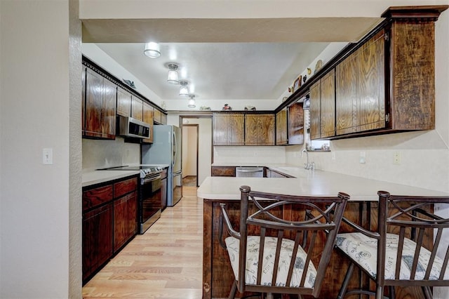 kitchen featuring light countertops, light wood-type flooring, appliances with stainless steel finishes, a peninsula, and a sink