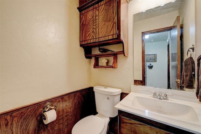 half bathroom featuring a wainscoted wall, toilet, wood walls, and vanity