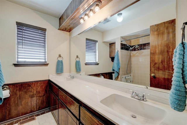 full bathroom featuring a wainscoted wall, tiled shower, visible vents, and a sink