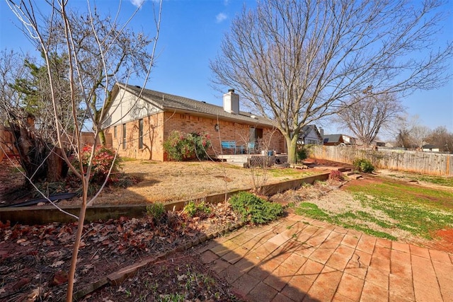 back of house featuring brick siding, a chimney, a patio, and fence