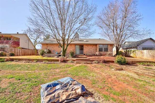 rear view of house with brick siding, a chimney, a yard, and fence