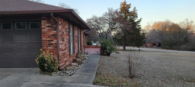 view of property exterior featuring a garage, brick siding, and roof with shingles