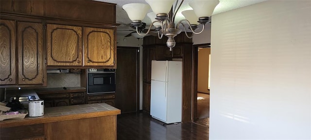 kitchen with a notable chandelier, tile counters, brown cabinetry, freestanding refrigerator, and black oven