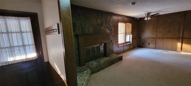 carpeted living room featuring ceiling fan, a textured ceiling, and a stone fireplace