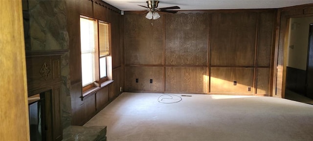 empty room with a large fireplace, a ceiling fan, and wooden walls