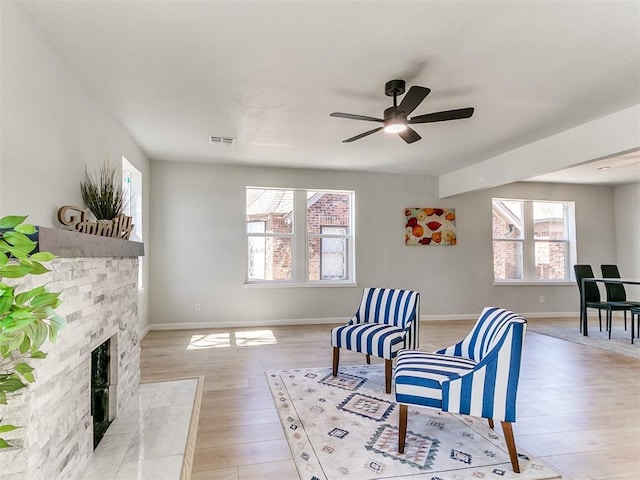 sitting room featuring a stone fireplace, light wood-style flooring, visible vents, a ceiling fan, and baseboards