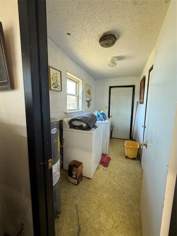 laundry room with laundry area, washing machine and dryer, a textured ceiling, and electric water heater