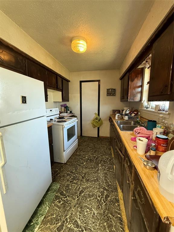 kitchen with a textured ceiling, dark brown cabinets, white appliances, and a sink