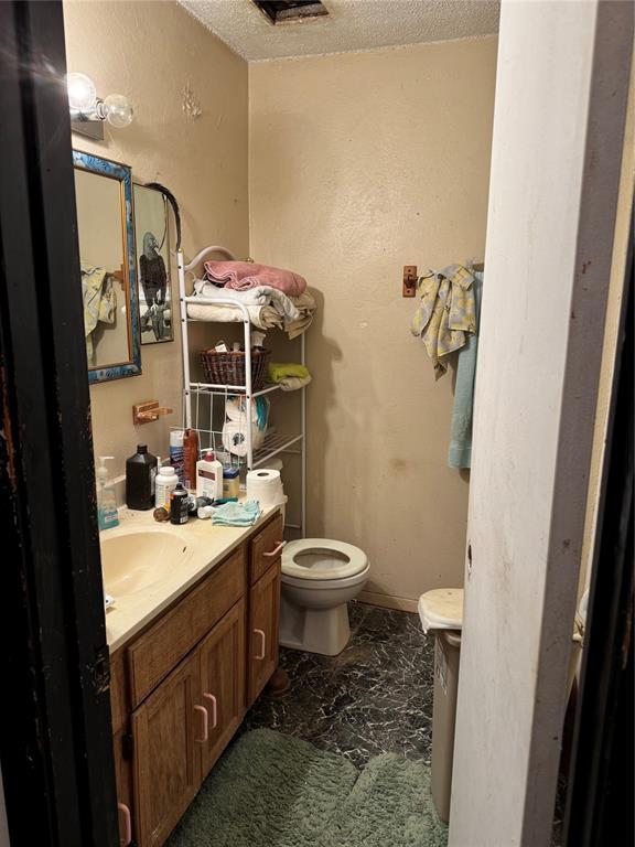 bathroom with marble finish floor, a textured ceiling, toilet, and vanity