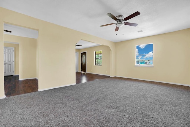 spare room with baseboards, dark carpet, arched walkways, and a ceiling fan