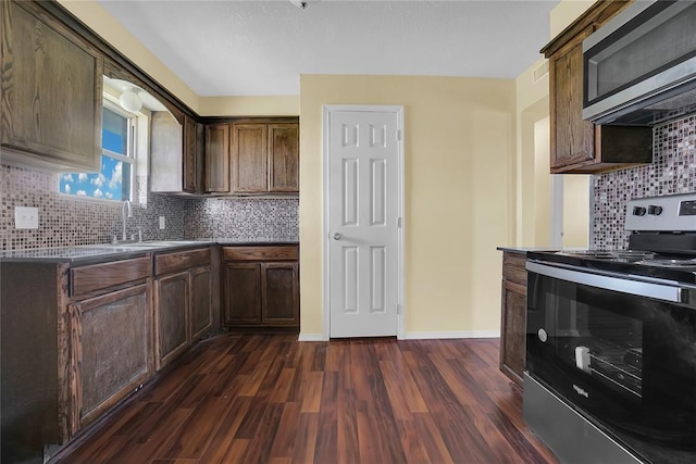 kitchen featuring dark wood finished floors, decorative backsplash, appliances with stainless steel finishes, a sink, and baseboards