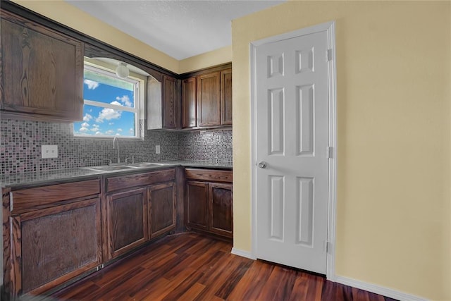 kitchen with tasteful backsplash, dark wood-type flooring, a sink, and baseboards