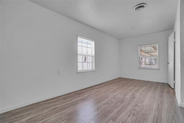 spare room featuring visible vents, plenty of natural light, baseboards, and wood finished floors