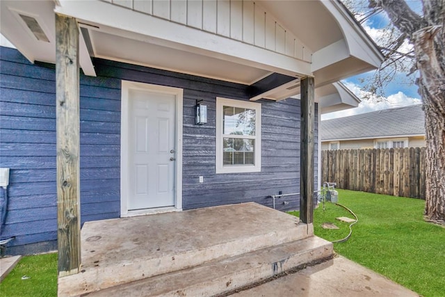 view of exterior entry with a lawn and fence