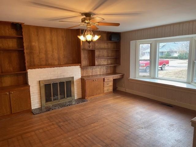 unfurnished living room with wood walls, a brick fireplace, a wall mounted AC, and a ceiling fan