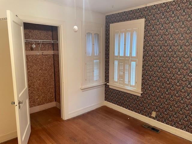 interior space with wallpapered walls, baseboards, visible vents, dark wood-style floors, and crown molding