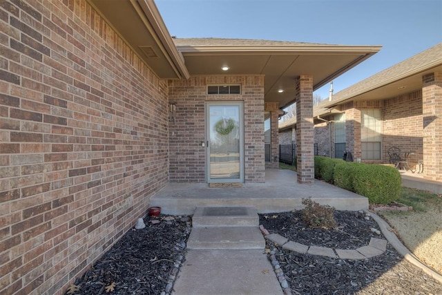 view of exterior entry featuring a patio and brick siding