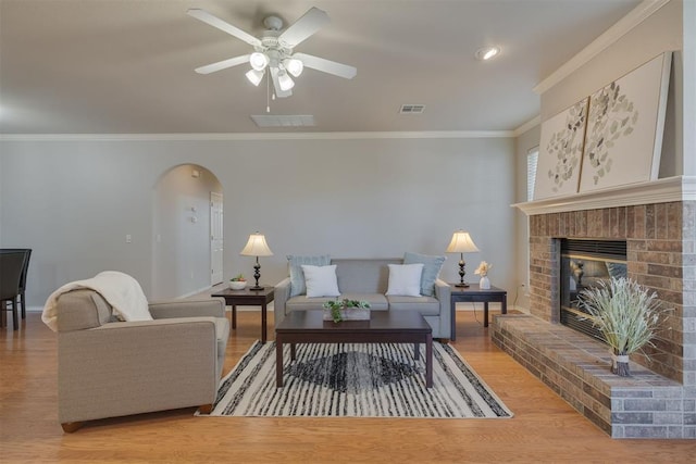 living room featuring wood finished floors, visible vents, a fireplace, arched walkways, and crown molding