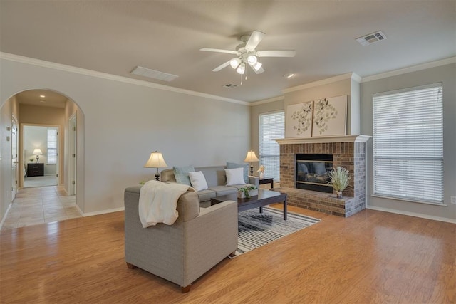 living room with light wood-style floors, a brick fireplace, visible vents, and arched walkways