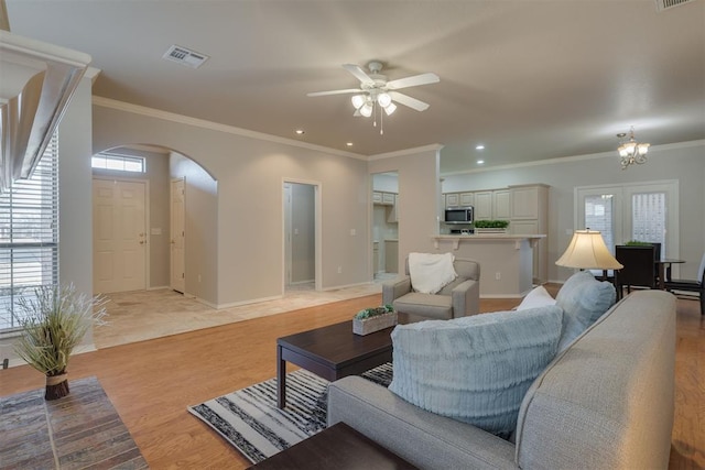 living room featuring visible vents, baseboards, arched walkways, light wood-style floors, and crown molding