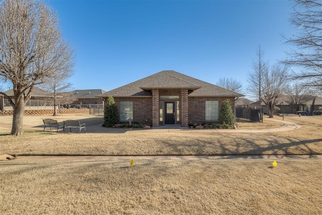 view of front of home with brick siding, a shingled roof, a front yard, and fence