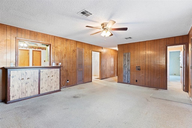 carpeted empty room featuring wooden walls, visible vents, ceiling fan, and a textured ceiling