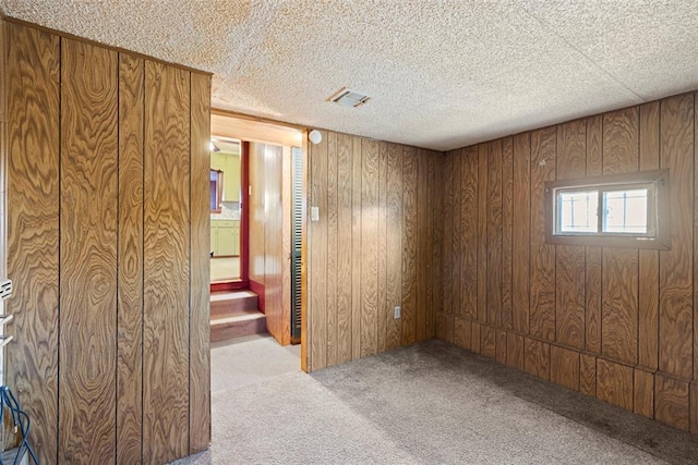 unfurnished room with a textured ceiling, stairway, carpet flooring, and wooden walls