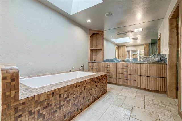 full bathroom featuring a skylight, recessed lighting, stone tile flooring, vanity, and a bath