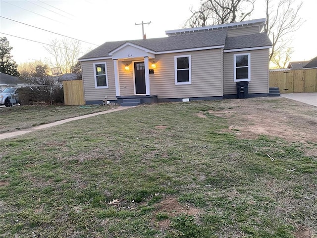 bungalow-style home featuring a shingled roof, fence, and a front lawn