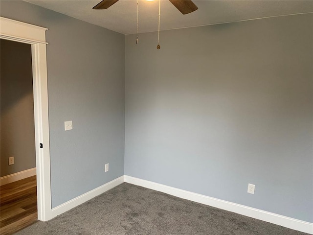 empty room featuring dark colored carpet, a ceiling fan, and baseboards