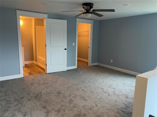 unfurnished bedroom featuring carpet floors, a walk in closet, ceiling fan, and baseboards