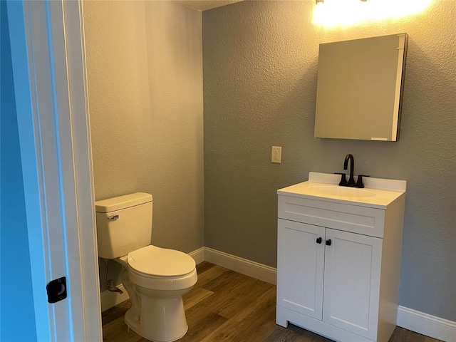 half bath with baseboards, a textured wall, toilet, wood finished floors, and vanity