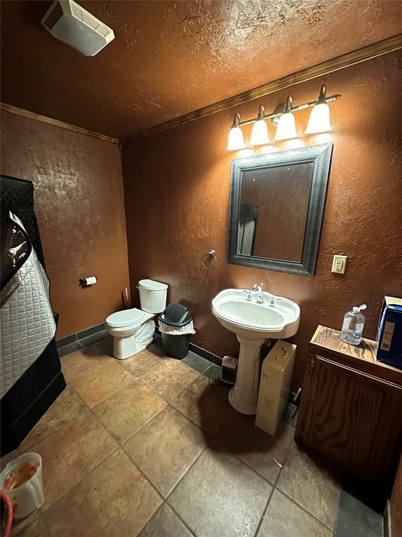 half bathroom with a textured ceiling, a textured wall, toilet, baseboards, and crown molding