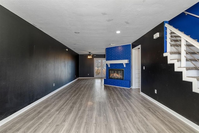 unfurnished living room featuring ceiling fan, a fireplace, wood finished floors, baseboards, and stairs