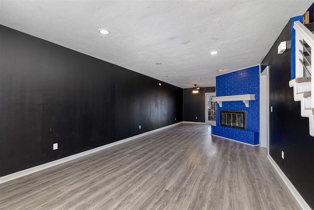 unfurnished living room featuring a brick fireplace, ceiling fan, baseboards, and wood finished floors