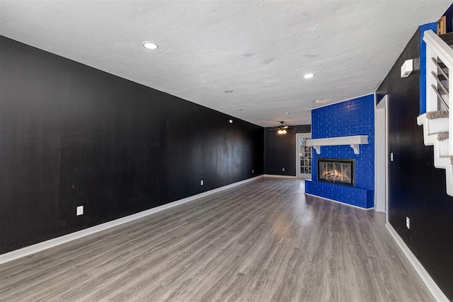 unfurnished living room featuring a ceiling fan, a brick fireplace, baseboards, and wood finished floors