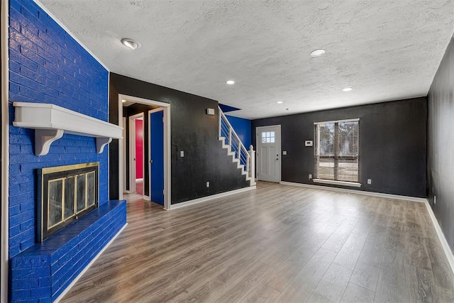 unfurnished living room with baseboards, wood finished floors, stairs, a textured ceiling, and a fireplace