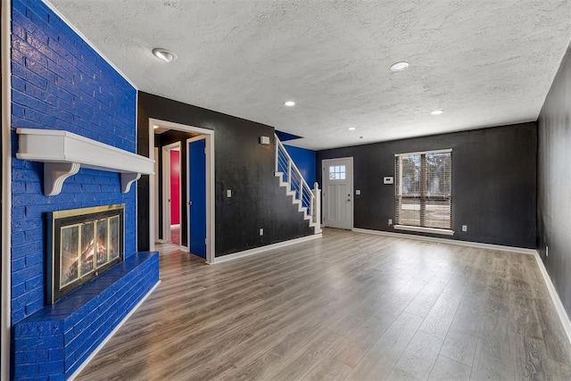 unfurnished living room featuring a textured ceiling, a fireplace, wood finished floors, baseboards, and stairway