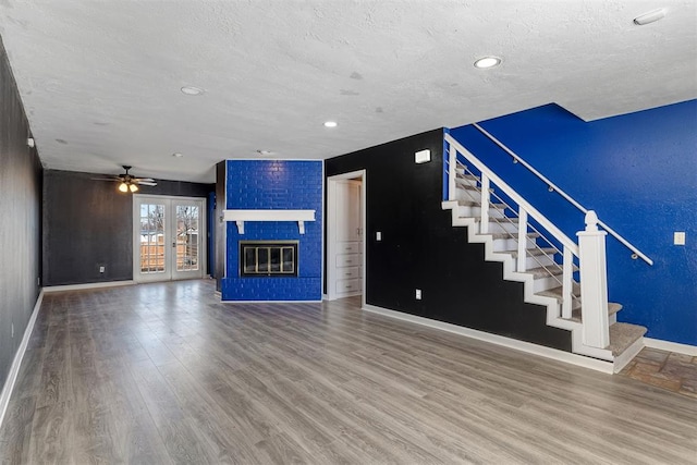 unfurnished living room with stairs, a textured ceiling, a fireplace, and wood finished floors