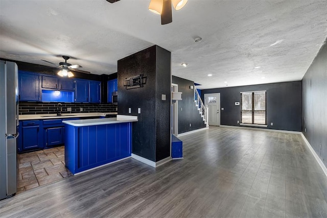 kitchen with blue cabinets, a sink, open floor plan, light countertops, and freestanding refrigerator