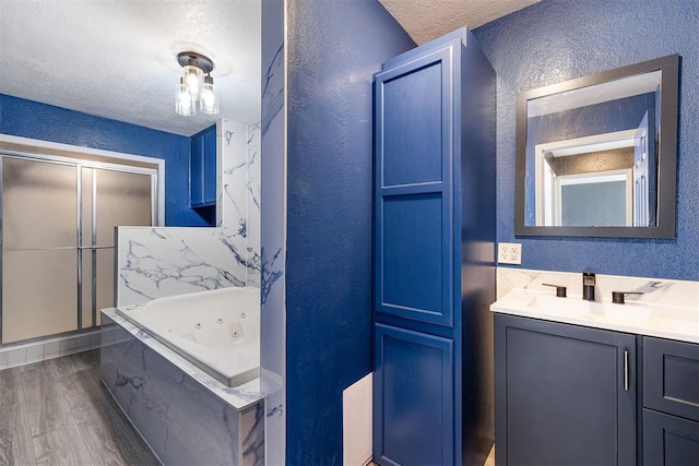 full bathroom featuring a textured wall, a tub with jets, wood finished floors, a textured ceiling, and vanity