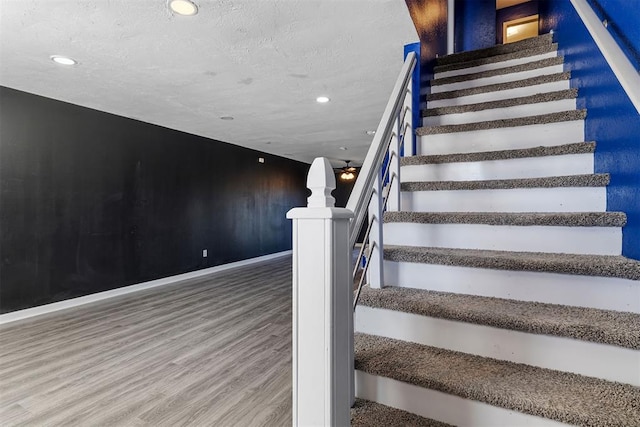 staircase with a textured ceiling, recessed lighting, wood finished floors, and baseboards