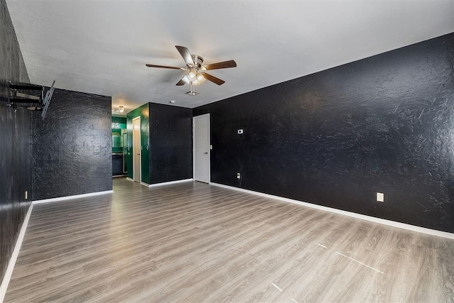 spare room featuring a textured wall, wood finished floors, a ceiling fan, and baseboards