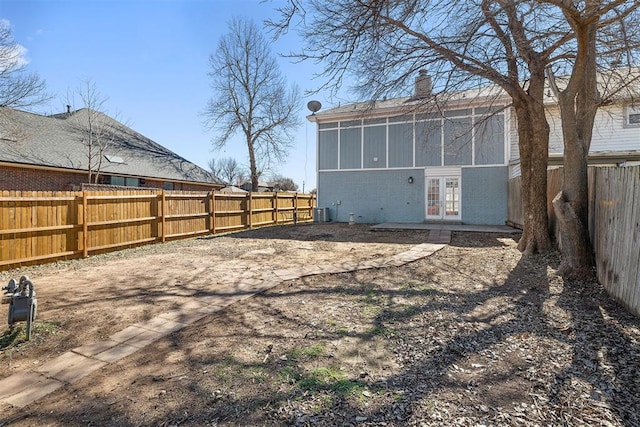 rear view of house with a fenced backyard, central AC, brick siding, french doors, and a chimney