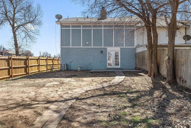 rear view of house with a fenced backyard, cooling unit, brick siding, a sunroom, and french doors