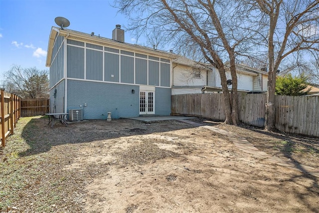 back of house with a fenced backyard, a chimney, french doors, central AC, and brick siding