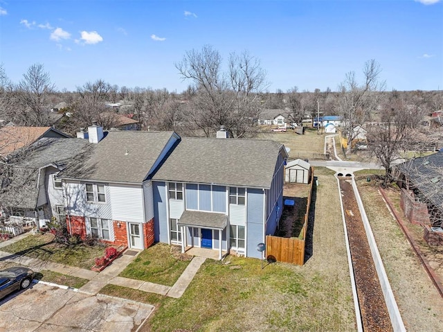 exterior space featuring roof with shingles, brick siding, a chimney, and fence