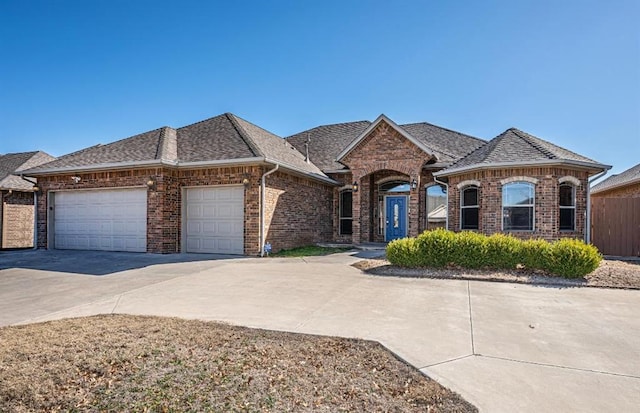 french country home with concrete driveway, brick siding, an attached garage, and roof with shingles