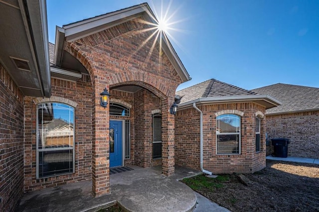 doorway to property featuring brick siding and roof with shingles