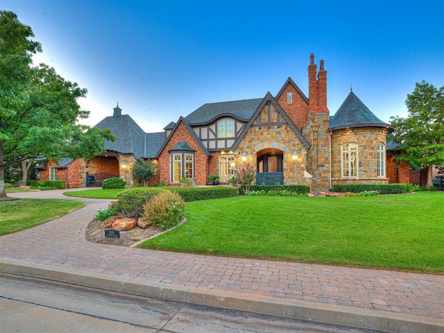 tudor-style house with a front yard, decorative driveway, and a chimney